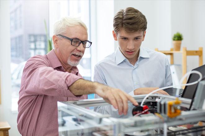 Elderly man pointing at an object and talking to a younger man with brown hair next to him