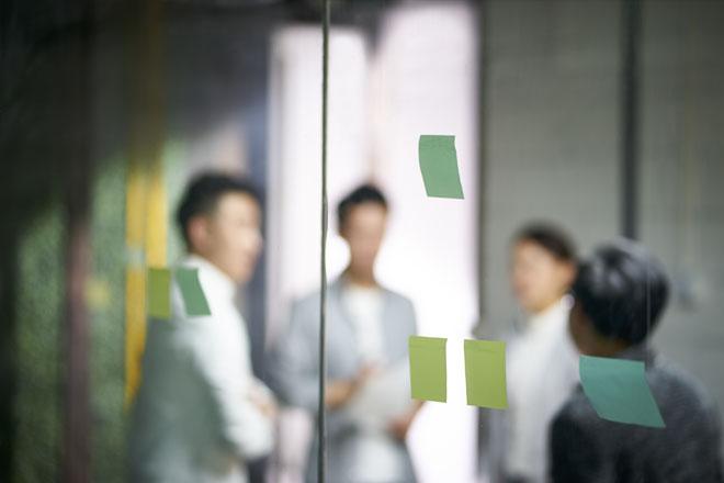 Blurry image of a group of four people in the background behind a pane of glass with blank post-it notes
